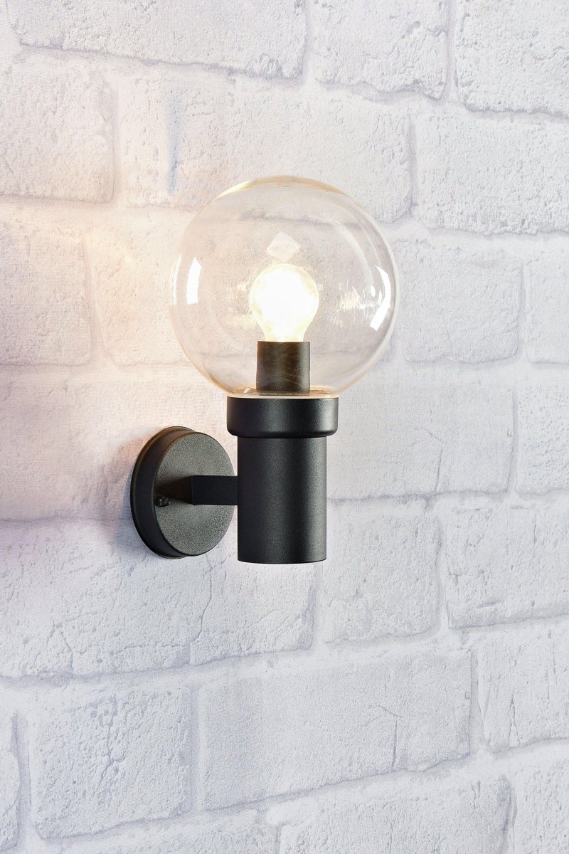 Caris Schwarz außenlampe Von Markslöjd - Mit einem robusten, schwarzen Metallsockel und einem gro&szlig;en, klaren Glasschirm verbreitet die Leuchte ein klares und angenehmes Licht, das eine einladende Atmosph&auml;re schafft.