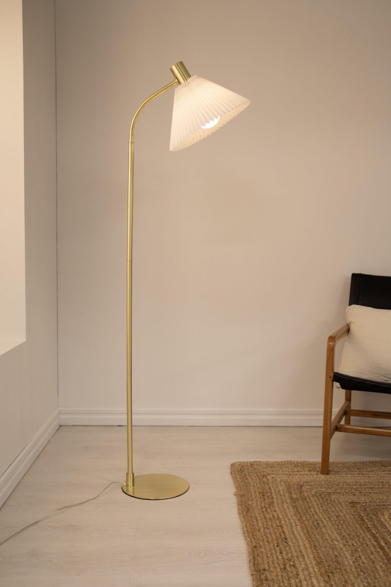 Mira Gebürstetes Messing stehlampe Von Markslöjd - Die Stehleuchte Mira ist 145 cm hoch, hat einen messingfarbenen Lampenfuß aus Metall und einen plissierten Lampenschirm aus weißem Stoff.