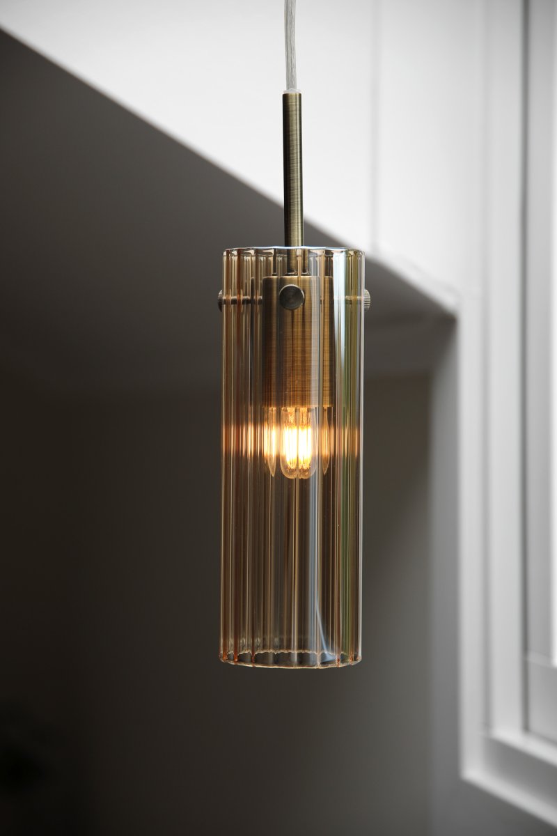 Tibia Ø7 Bernstein/Messing fensterlampe Von Markslöjd - Zylindrische Fensterleuchte aus geriffeltem, bernsteinfarbenem Glas mit eleganten Messingdetails – ein warmes und dekoratives Design, das ein sanftes, stimmungsvolles Licht im Fenster erzeugt.