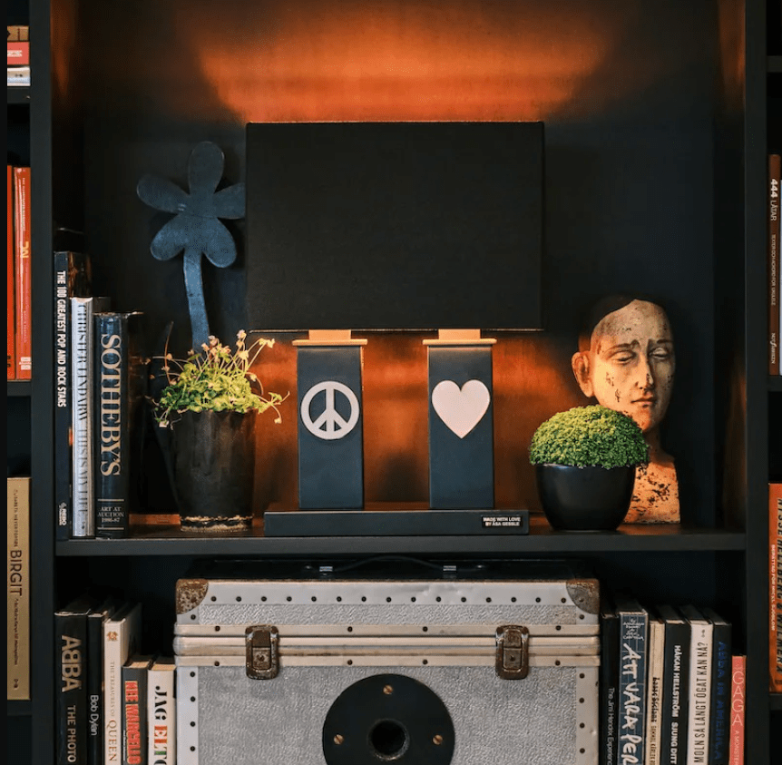 Stand By Me 50cm Schwarz tischlampe Von By Rydéns - Der breite, schwarze Stofflampenschirm harmoniert im Kontrast mit den schmaleren S&auml;ulen des Lampenfu&szlig;es, die beide mit einem Metallsymbol verziert sind, auf der einen Seite dem Peace-Zeichen, auf der anderen einem Herz.