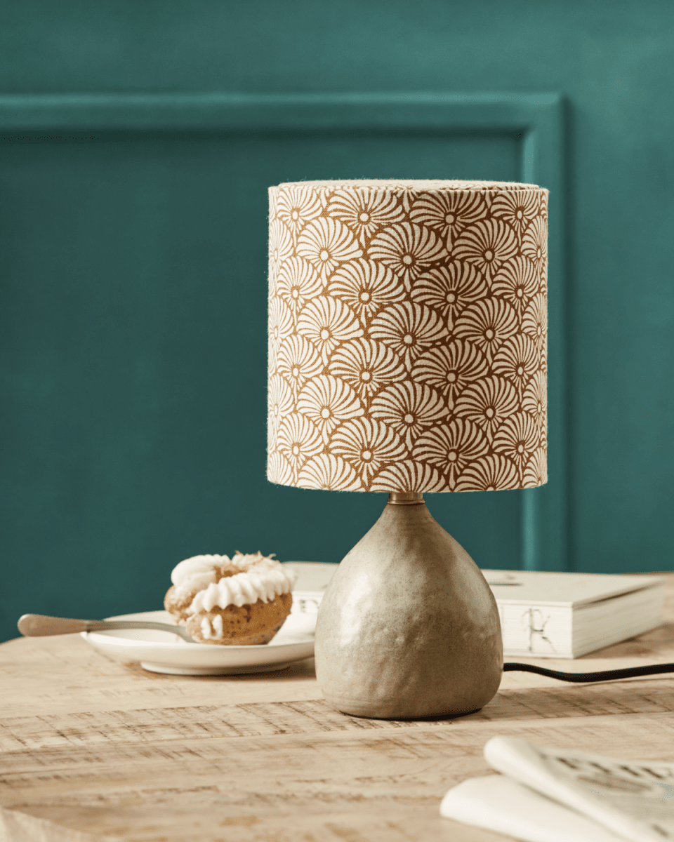 Flores 30cm Sand tischlampe Von House Doctor - Es verfügt über einen sandfarbenen Keramiksockel und einen Lampenschirm aus Leinen, der mit handgedruckten sand- und braunen Sonnenfedermotiven verziert ist und so eine moderne und gemütliche Ästhetik auf wunderbare Weise in Einklang bringt.