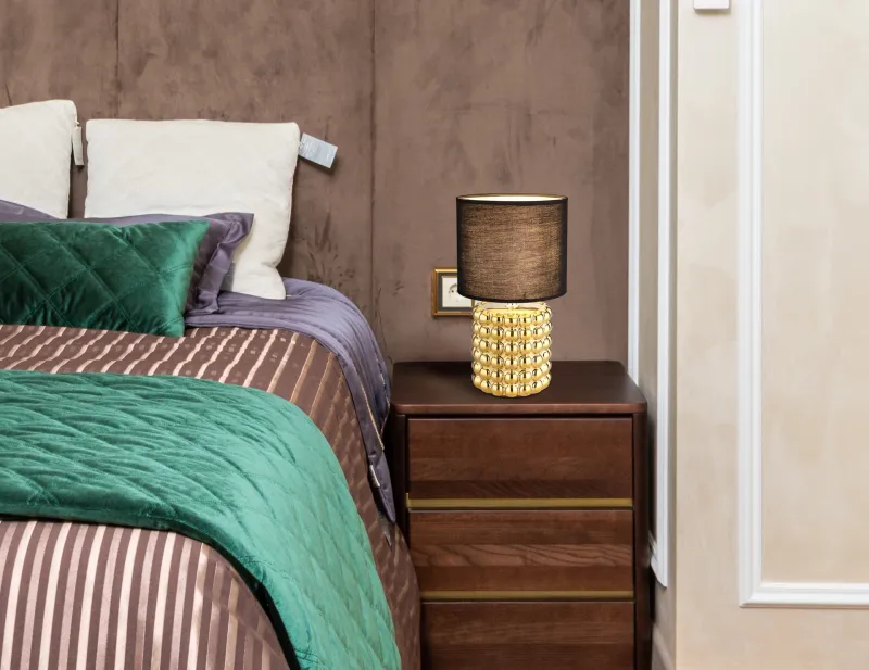 Valentino 33cm Gold tischlampe Von Globo Lighting - P&aring; en cylinderformad fot i guldf&auml;rgad keramik vilar en stilren, svart textilsk&auml;rm.