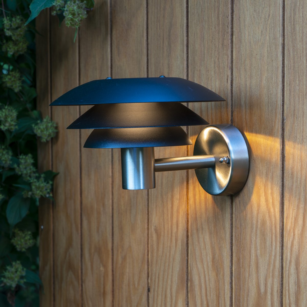 DL20 Edelstahl außenlampe Von Dyberg Larsen - Die Lampe verfügt über drei ikonische Schirme in unterschiedlichen Größen, die ein magisches Licht verbreiten und ist aus Edelstahl mit eleganten mattschwarzen Schirmen gefertigt.