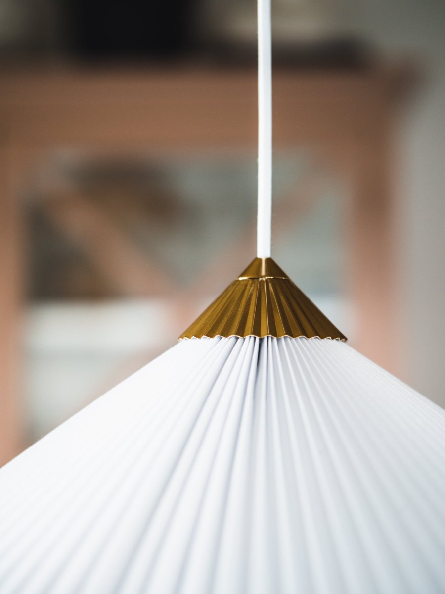 Matisse Ø60 Weiß hängelampe Von Globen Lighting - Die Lampe hat einen plissierten weißen Textilschirm und ist mit einem dazu passenden plissierten Oberteil aus messingfarbenem Metall verziert.