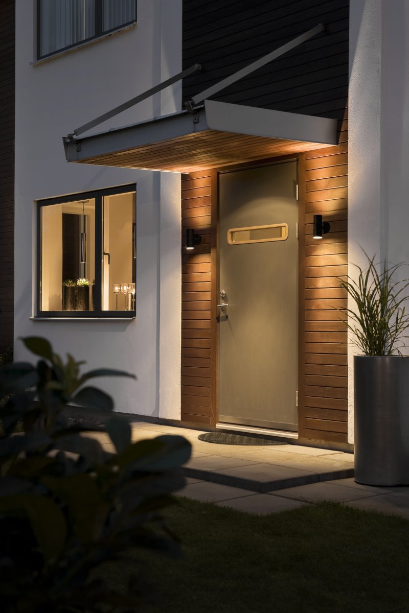 Modena Schwarz außenlampe Von Konstsmide - Die Leuchte strahlt das Licht nach oben und unten ab und erzeugt ein dekoratives Lichtbild, das die Fassade hervorhebt und eine einladende Atmosph&auml;re im Au&szlig;enbereich schafft.