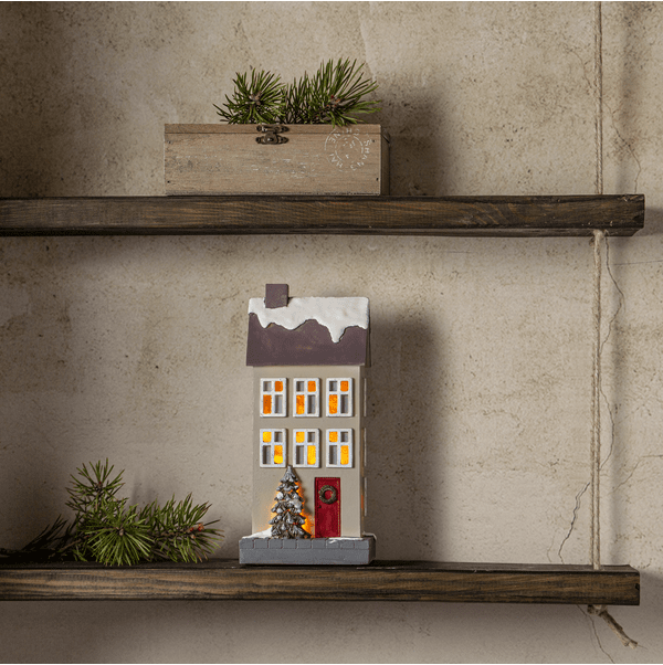 Hus 24cm Beige Von Star Trading - Beige Hauslaterne mit warmem, gelbem Licht, das durch die Fenster scheint.